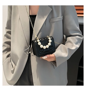 Detail of mini black quilted crossbody bag with pearl handle and golden chain strap
