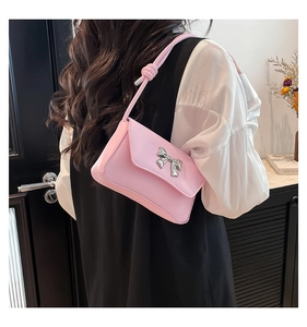 Close-up of pink shoulder bag featuring a silver metal bow detail in a cozy home setting
