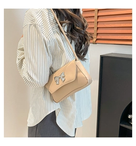 Close-up of beige shoulder bag with silver butterfly metal ornament on a female model
