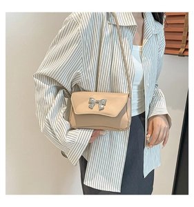 Detail of beige rectangular shoulder bag with a silver metal bow accent on casual outfit
