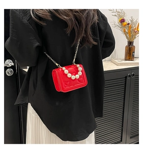 Detail of red heart-quilted mini crossbody bag with pearl handle and gold chain strap