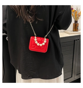 Detail of red heart-quilted mini bag with pearl handle and gold chain strap on model