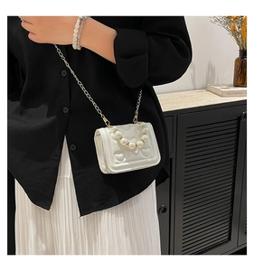 Detail of white heart-quilted mini bag with pearl handle and golden chain strap