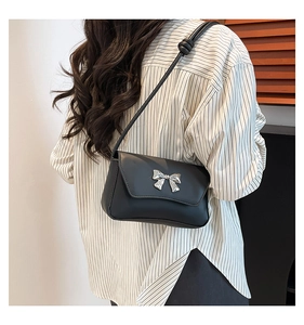 Close-up of matte black baguette bag with silver metal bow detail on a shoulder strap