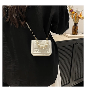Detailed view of white heart-quilted mini bag with large pearl handle and gold chain strap