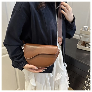 Close-up of brown leather saddle bag with wide fabric strap worn by a model