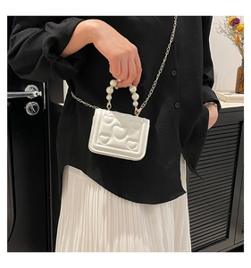 Close-up of white heart-quilted mini bag featuring pearl handle and gold chain strap