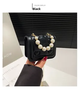 Detail of black quilted heart mini bag featuring glossy finish and pearl chain handle