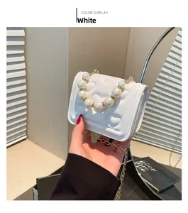 Detail of white quilted handbag with heart patterns, pearl handle, and gold chain strap