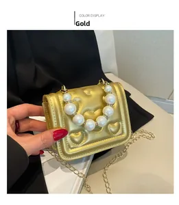 Detail of heart-quilted gold mini bag featuring large pearl handle and gold chain strap