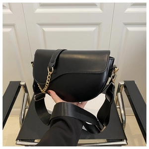 Detail of black saddle bag featuring gold chain link and wide nylon shoulder strap