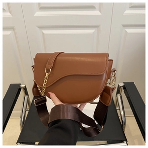 Close-up of brown saddle bag featuring asymmetric curved flap and golden chain detail