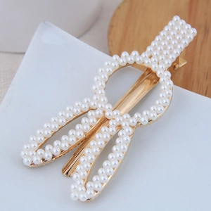 Détail d'une barrette dorée ornée de perles blanches serties sur un motif géométrique chic