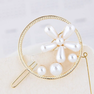 Détail d'une pince à cheveux ronde dorée avec fleur de perles et texture métallique tressée