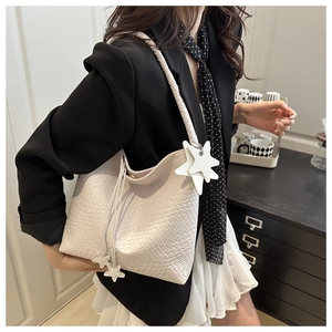 Dettaglio della borsa tote in pelle intrecciata crema con ciondolo a stella sulla spalla