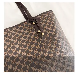 Detail view of brown monogram tote bag with gold M-logo pendant and premium leather texture