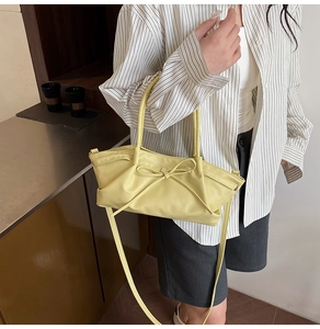 Close-up of a light yellow tote bag with bow detail held by a model in a warm setting