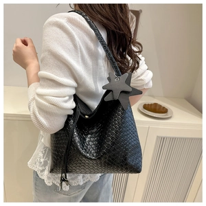 Détail du sac cabas noir en cuir tressé avec pendentif étoile porté à l'épaule du modèle