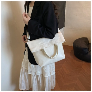 White faux leather tote bag with wide strap and folding flap shown on model