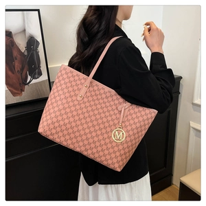 Detail of pink monogram tote bag with golden charm shown on shoulder for capacity