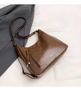 Detail view of brown matte leather shoulder bag with side tassel zipper and adjustable strap