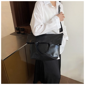 Detail of a large black leather tote bag worn by a model in a minimalist indoor setting
