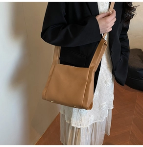 Detail of tan lychee grain leather crossbody bag with gold rivets and embossed logo