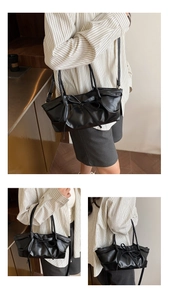 Close-up of black pleated PU shoulder bag with bow detail and adjustable straps