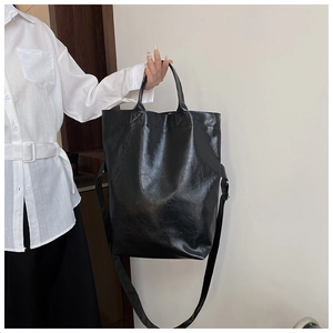 Detail showing the shiny black PU leather texture and wide strap of the large tote bag