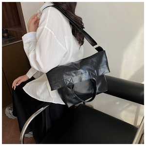 Modern black glossy large tote bag with crossbody strap shown in a minimalist interior