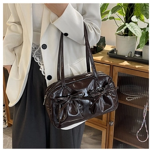 Detail of a glossy dark brown shoulder bag featuring bow accents and pleated oil wax finish