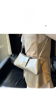 Détail du sac baguette argenté avec boucle dorée géométrique et bandoulière en cuir