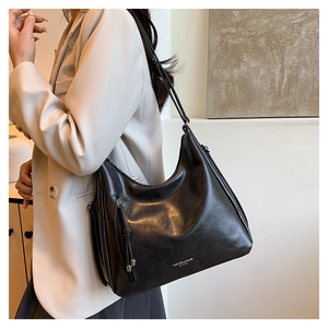Detail of black leather shoulder bag showing elegant tassels and side zipper texture