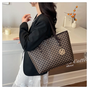 Detail of a brown monogram tote bag with gold M-logo charm and leather shoulder strap