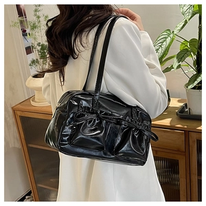 Dettaglio di una borsa a spalla nera lucida con fiocco decorativo e sottili tracolle
