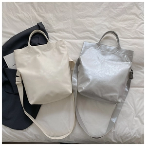 Detail showing cream and silver leather tote bags with adjustable straps on fabric background
