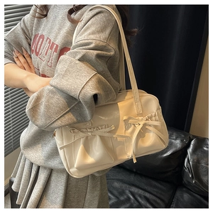 Detail of cream glossy leather baguette bag featuring stylish bow-tie pleat pockets