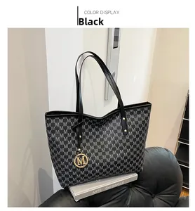 Detail of black tote bag with gray M monogram pattern and golden M logo charm pendant
