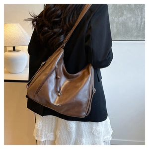 Detail of dark brown leather tote bag with side zippers and tassel on a female model