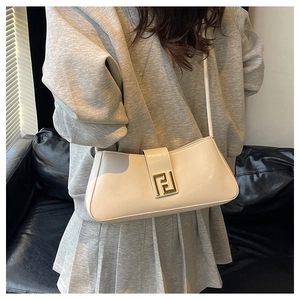 Gros plan d'un sac baguette en cuir verni beige avec boucle dorée porté par un mannequin