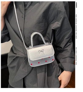 Détail du sac à main argenté à nœud et pois rouges porté en bandoulière par un mannequin