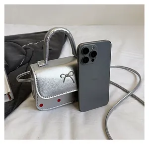Mini sac argenté à pois avec nœud métallique à côté d'un smartphone pour l'échelle