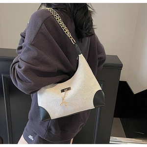 Detail view of large tote bag with cream fabric, black leather trim and deer charm