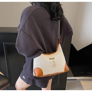 Detail of vintage canvas underarm bag with brown leather trim and golden deer charm