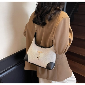 Detail of minimalist cream canvas tote bag with black leather trim and golden deer charm