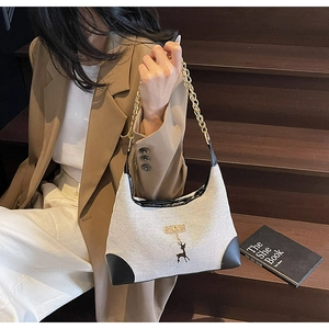 Detail of canvas tote bag with black leather corners and gold chain strap on wooden steps