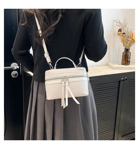Détail d'un sac seau blanc texturé avec fermetures éclair et pompons en cuir