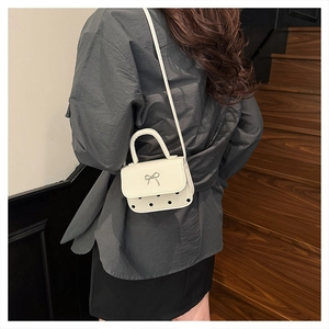 Detailed view of mini white crossbody bag with black polka dots and silver bow decoration