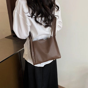 Dark brown leather bucket bag shown as a crossbody on a model with white shirt