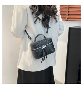 Détail du sac boîte noir en cuir tressé avec de longs pompons et fermeture zippée